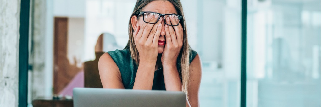 Woman rubbing eyes at desk.