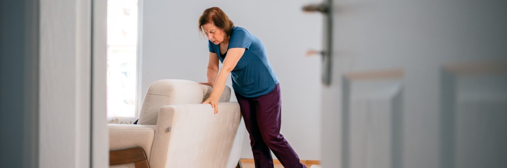 Woman pushing a sofa indoors.