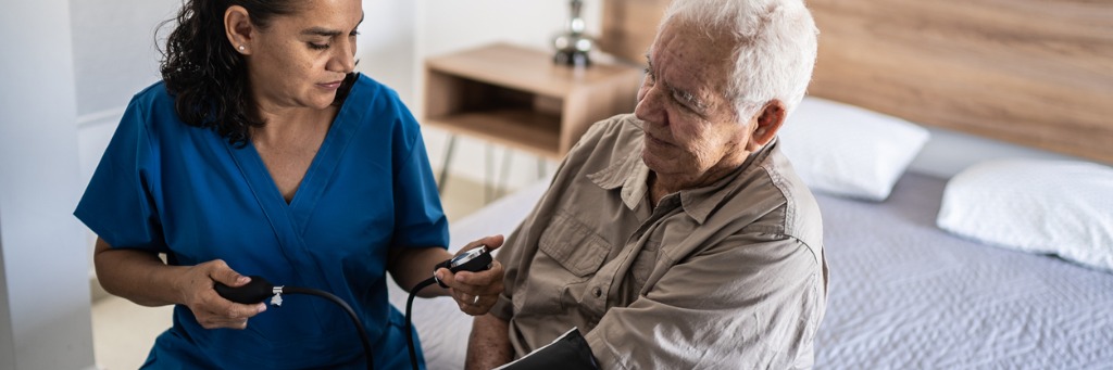 Nurse checking elderly man's blood pressure.