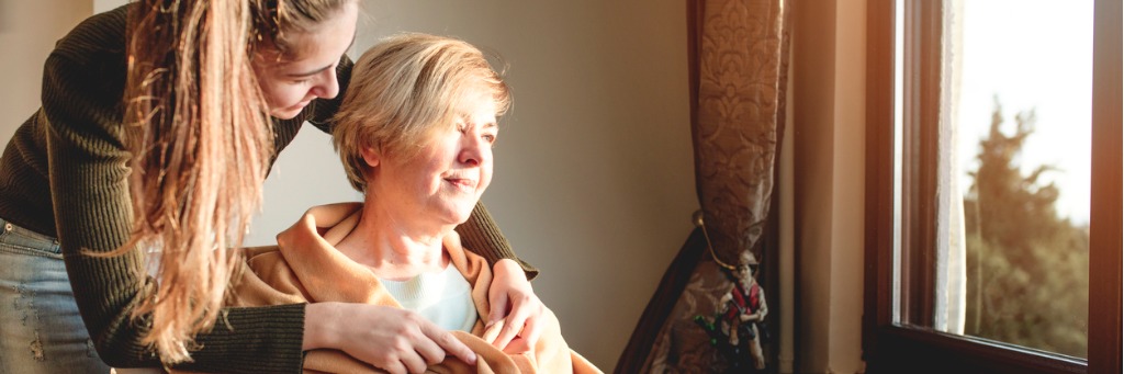 Woman comforting elderly woman by window.